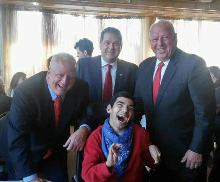 A guest laughing with three men in suits at an Operation Santa Claus event